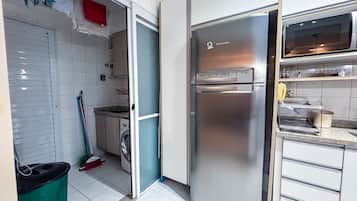 Cozinha equipada com geladeira de aço inoxidável, máquina de lavar e vassoura.
