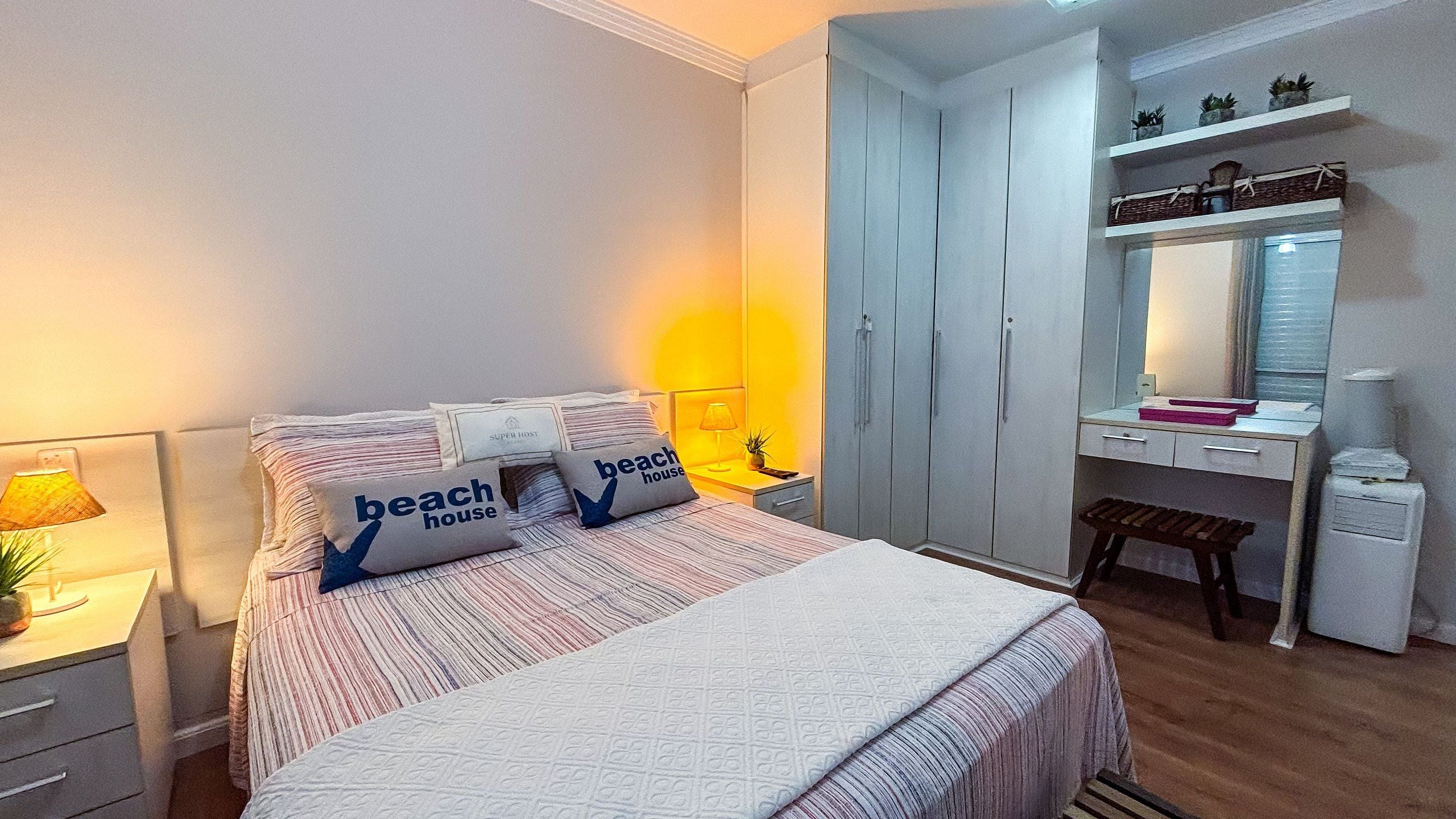 Quarto de hotel com cama, escrivaninha, guarda-roupa e prateleira com plantas.