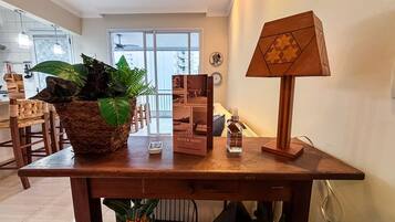 A wooden table with a woven basket of plants, a Super Host Brazil box, a remote control, and a lamp.