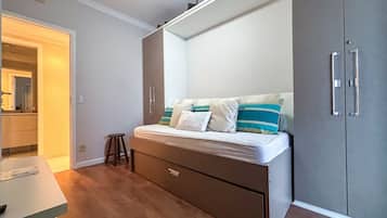 Un dormitorio compacto con cama, un taburete pequeño, un armario y una zona de kitchenette.