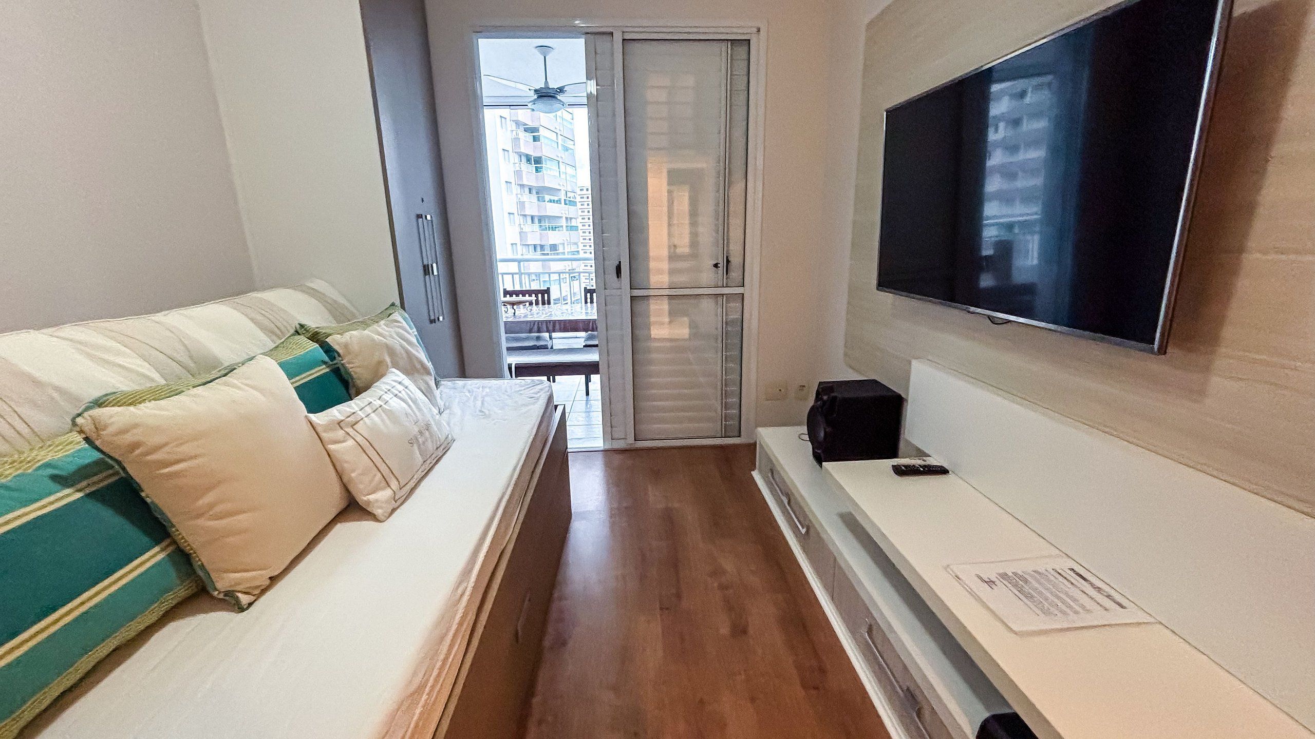 Et hotelværelse med en sofa, et fladskærms-tv, trægulv og en skydedør, der fører ud til en balkon.