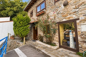 A stone building with a wooden door, a small garden with potted plants, and a window displaying miniature models.