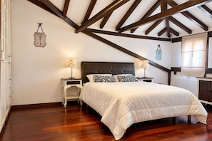 A bedroom with a wooden ceiling, a bed with white bedding, two bedside tables with lamps, and a window with curtains.
