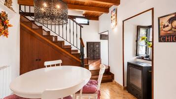 Un comedor con una mesa y sillas blancas, una escalera de madera y una zona de cocina con estufa.