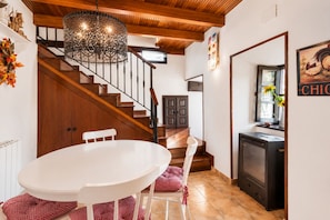 A dining area with a white table and chairs, a wooden staircase, and a kitchen area with a stove.