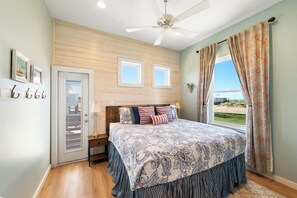 Ein Schlafzimmer mit einem Bett, einem Deckenventilator, einem Fenster mit Vorhängen und einer Tür mit einem Fenster.
