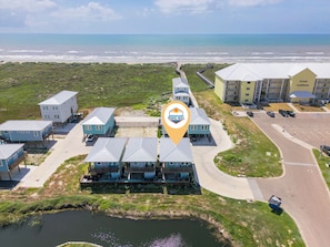 Vista aérea de un hotel costero con varias edificaciones, un estacionamiento y una playa al fondo.