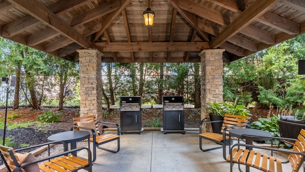 Eine Terrasse im Freien mit Steinpfeilern, Holzbalken und zwei Grillstationen.