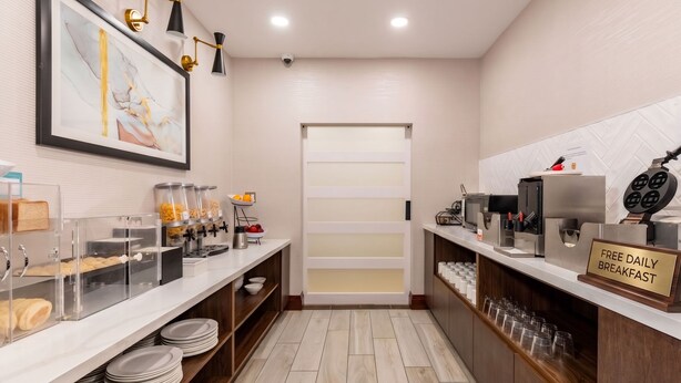 Ein Frühstücksbereich mit Schild, das kostenfreies Frühstück täglich anbietet, einer Kaffeemaschine und einem Waffelautomat.