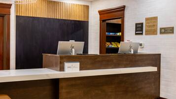 Un comptoir d’accueil avec deux ordinateurs portables HP, une enseigne indiquant « IHG One Awards », et une caméra de surveillance au-dessus.