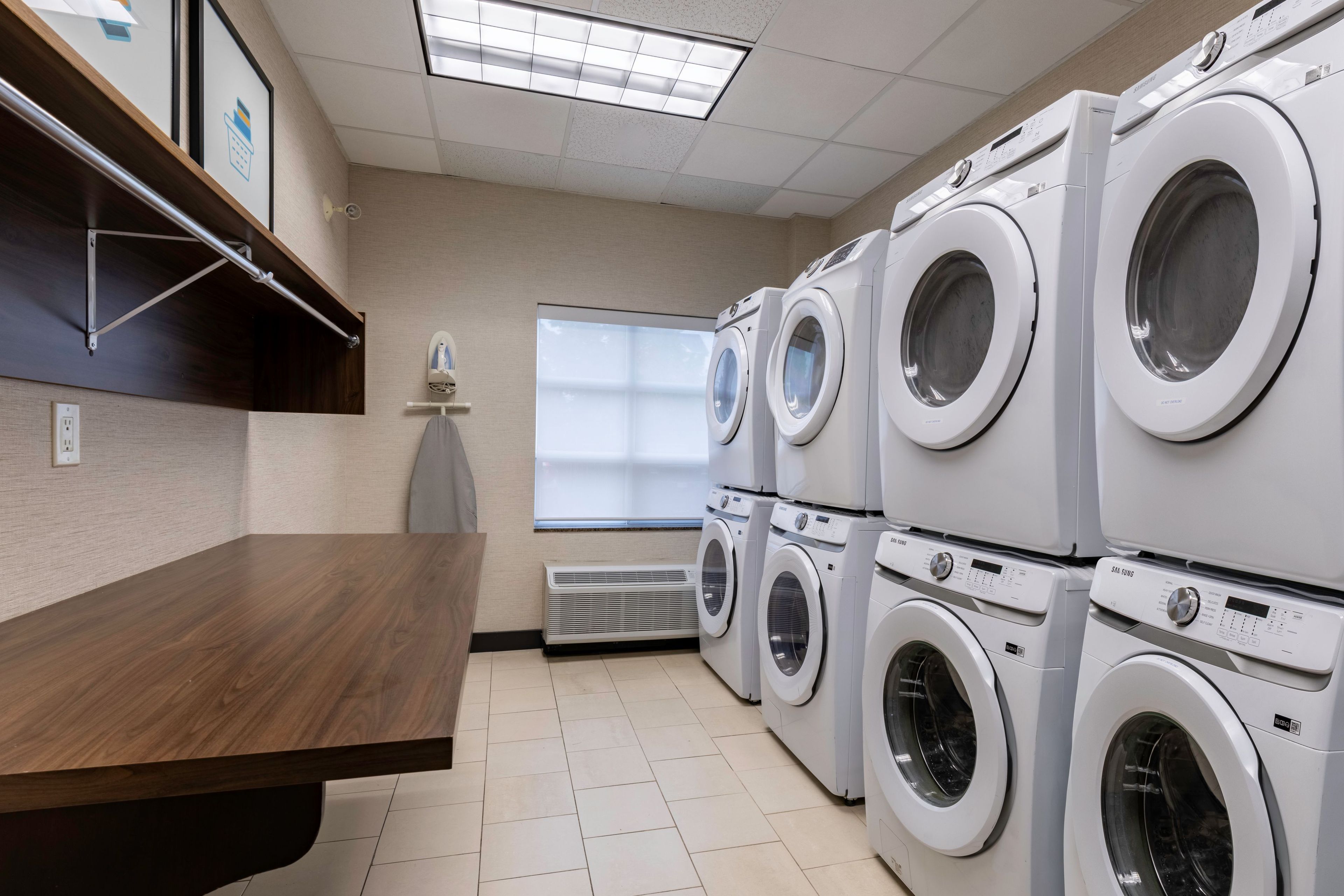 A laundry room with multiple washing machines, a wooden table, and a window with a view.