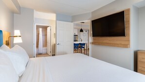 Ein Hotelzimmer mit Bett, Wandfernseher, Schreibtisch und Duschbereich.
