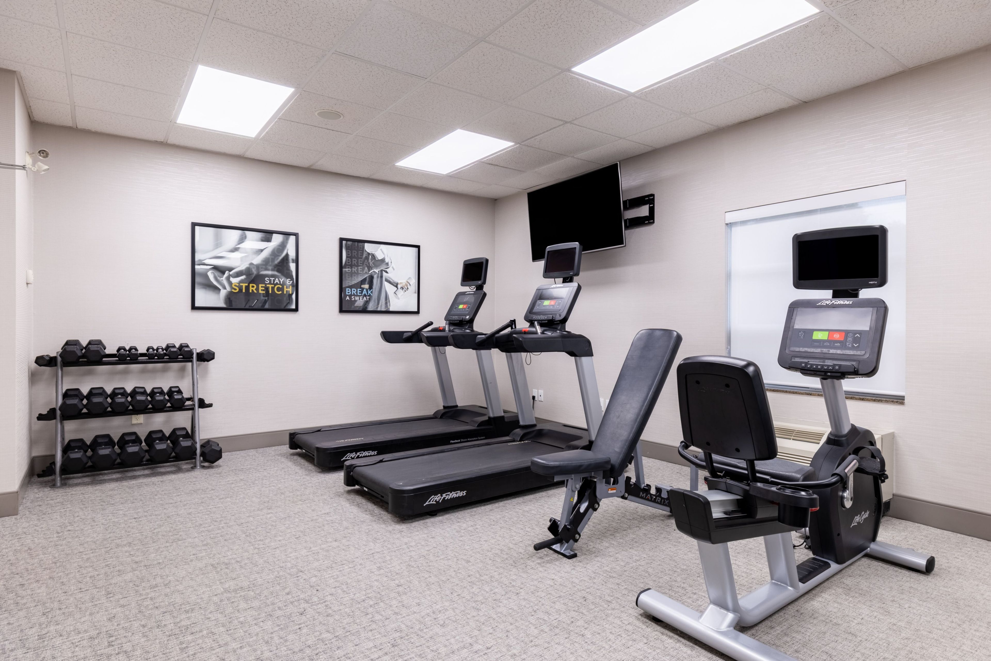 A fitness center with treadmills, an elliptical, and a dumbbell rack.