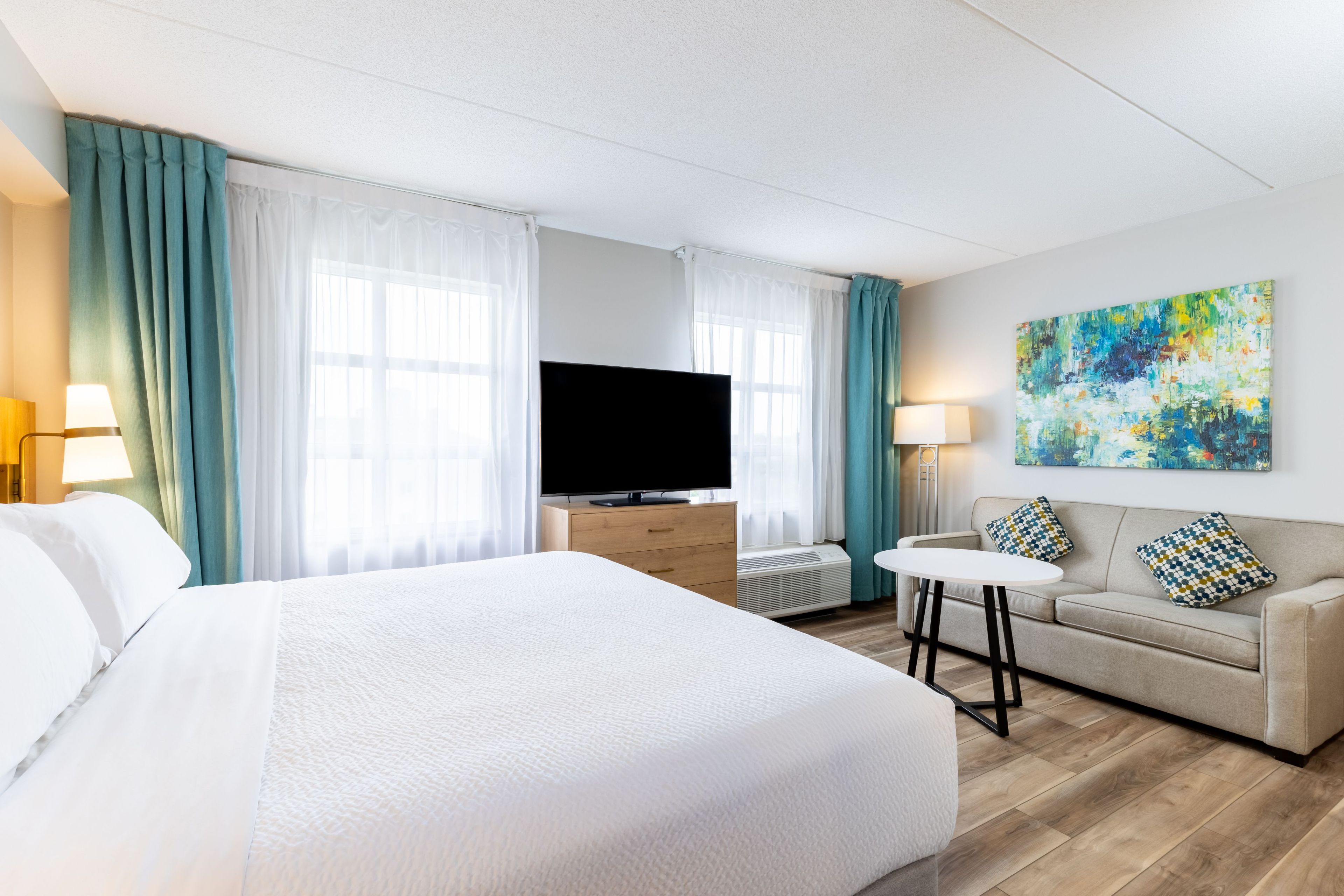 A hotel room with a large bed, a television, a sofa, and a painting on the wall.