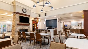 A restaurant with tables and chairs, a fireplace, a clock, and a kitchen area. - King Studio w/ Jetted Tub | Pool + Hot Breakfast (London)