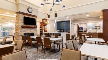 A restaurant with tables and chairs, a fireplace, a clock, and a kitchen area.