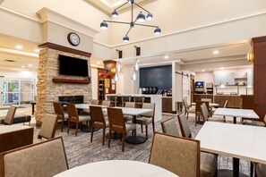 Un restaurant avec des tables et des chaises, une cheminée, une horloge et un espace cuisine.