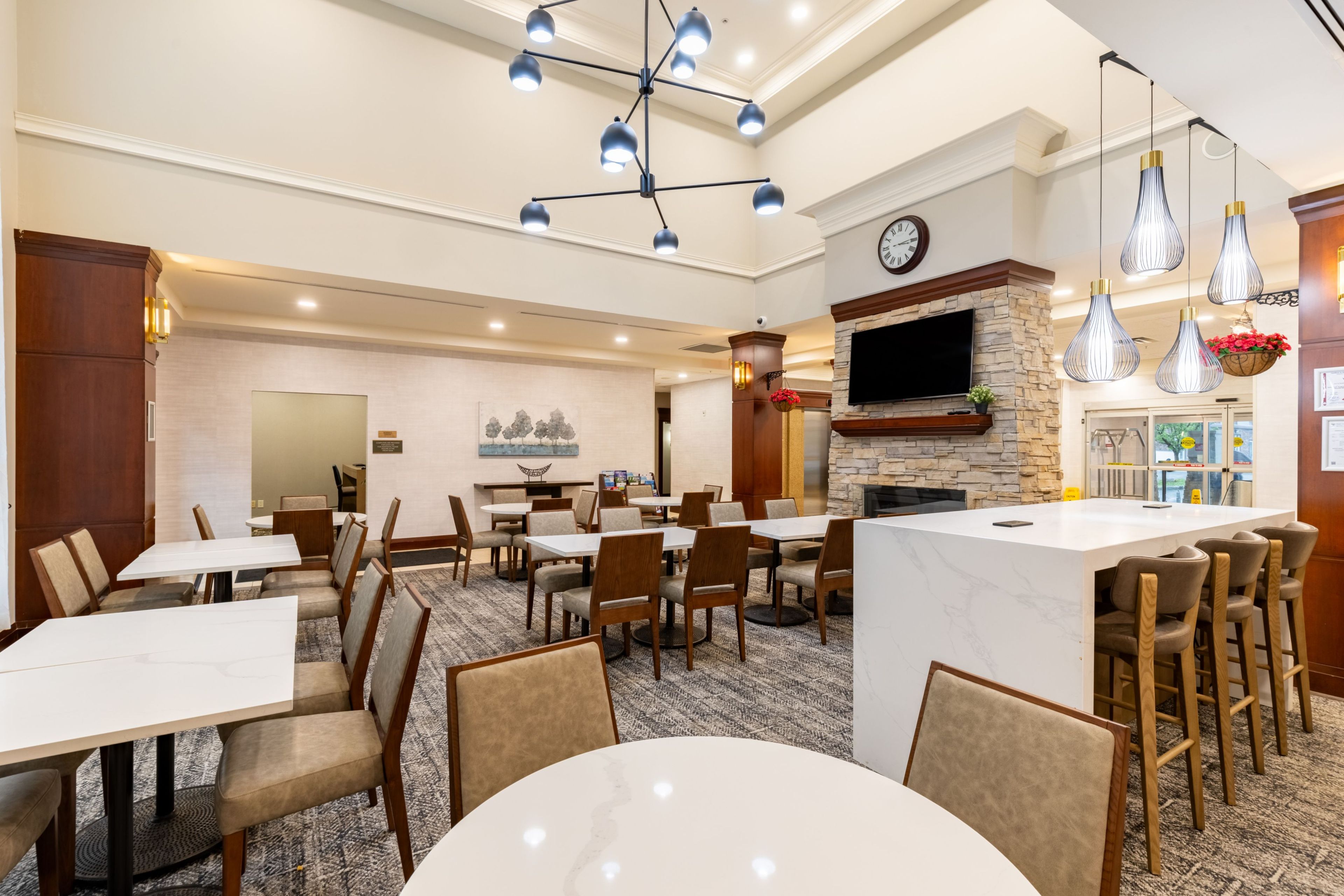 A hotel dining area with multiple tables and chairs, a fireplace, and a television mounted on the wall.