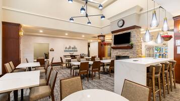 A hotel dining area with multiple tables and chairs, a fireplace, and a television mounted on the wall.