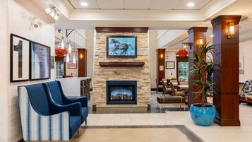 A lobby with a stone fireplace, blue sofas, a large potted plant, and framed artwork on the walls.