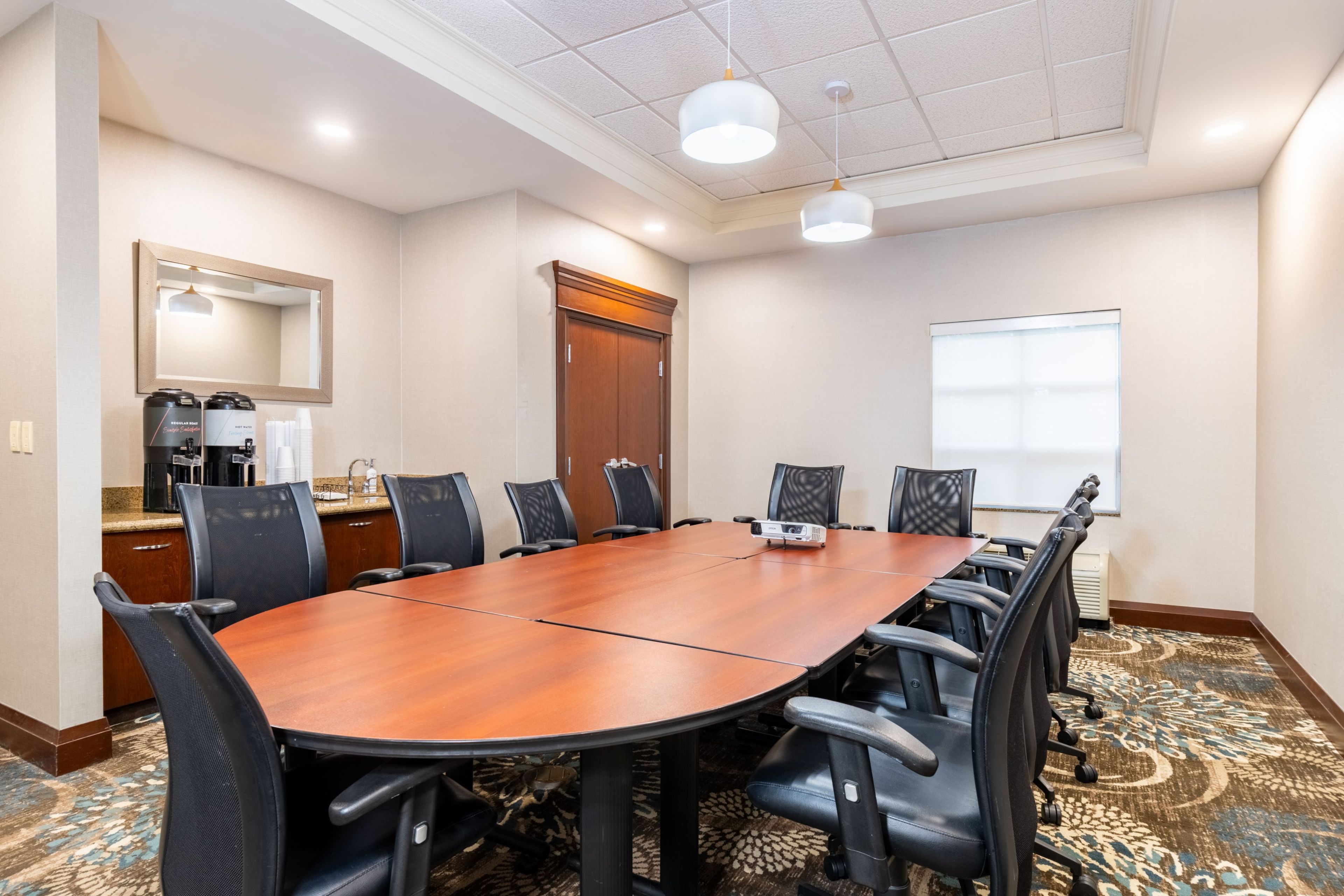 A conference room with a long table, chairs, a coffee station, and a large mirror on the wall.