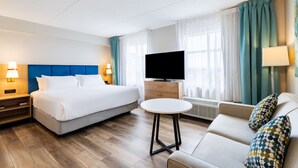 A hotel room with a bed, a sofa, a TV, a small table, and a window with curtains. - King Studio w/ Jetted Tub | Pool + Hot Breakfast (London)