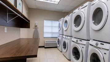 A laundry room with multiple washing machines, a wooden table, and a window with a view.