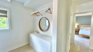 A bedroom with a white dresser, a round mirror, and a bed with a white headboard.