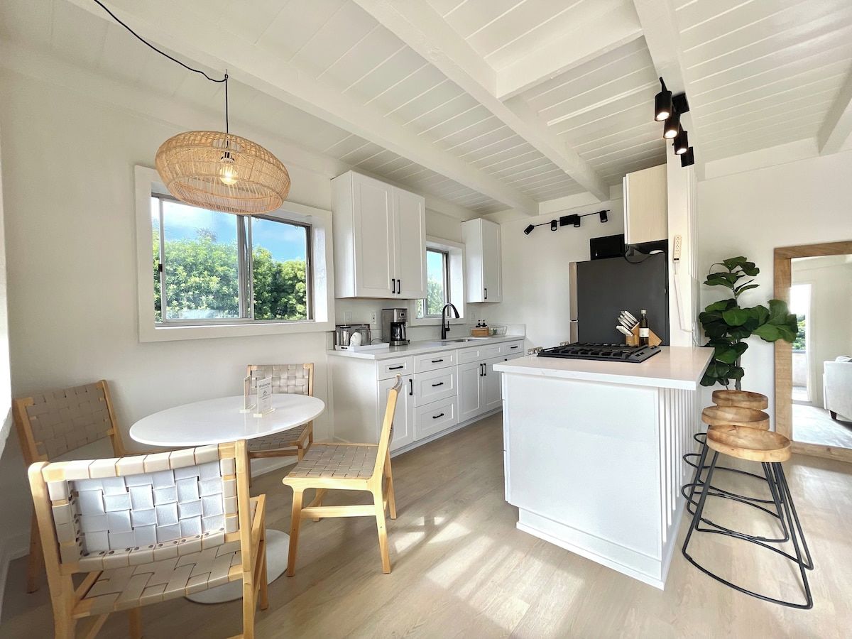 A modern kitchen with white cabinetry, a central island, and a dining area with a round table and chairs.