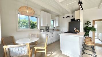 A modern kitchen with white cabinetry, a central island, and a dining area with a round table and chairs.