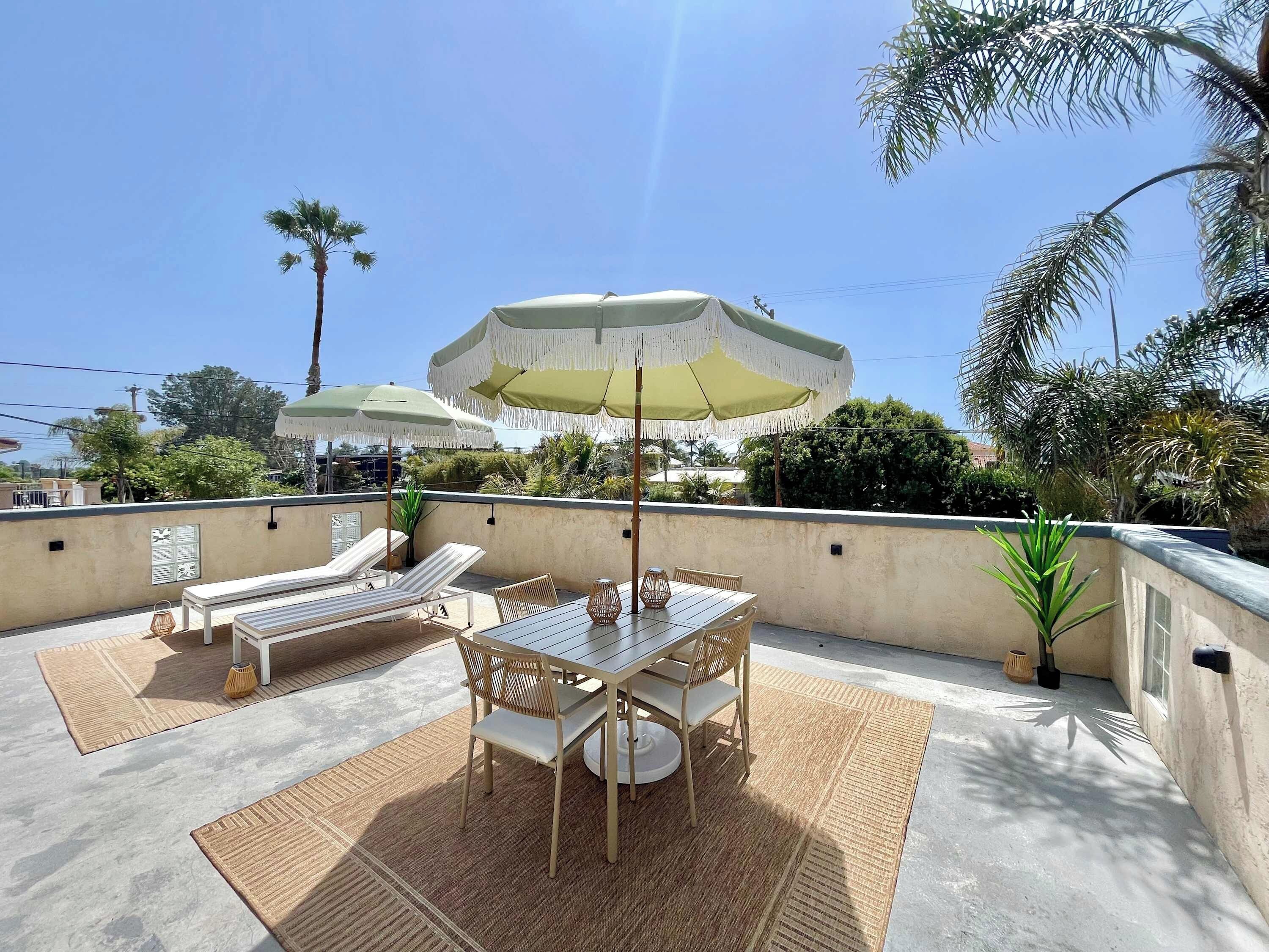 A rooftop patio with a table and chairs, two umbrellas, and lounge chairs.