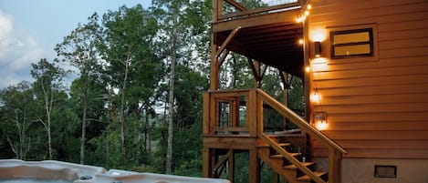 A wooden cabin with a hot tub, a deck, and a staircase leading to an upper level.