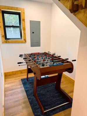 Une pièce avec une table de baby-foot en bois, une fenêtre et une porte.