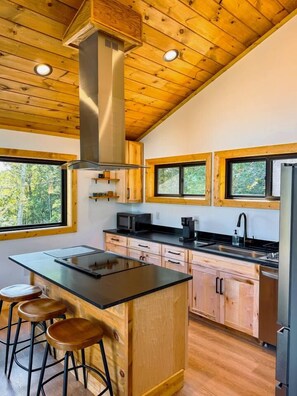 Une cuisine moderne avec des meubles en bois, un îlot central doté de tabourets et une hotte de cuisine en acier inoxydable.