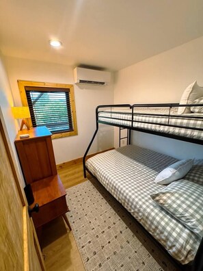 A bunk bed with a checkered bedspread, a bedside table with a lamp, and a window with blinds. - Mountaintop Cabin with Hot Tub, Decks & Grandfather Mountain Views (Linville)