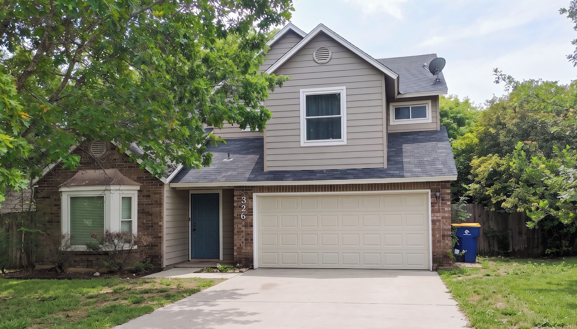 A two-story house with a garage, a brick section on the left, and a tree in the front yard.