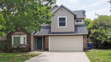 A two-story house with a garage, a brick section on the left, and a tree in the front yard.
