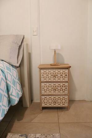A small wooden nightstand with a lamp, a patterned blanket on a bed, and a plain wall. - Casa Mirador, a jungle retreat near the beach (Baru)