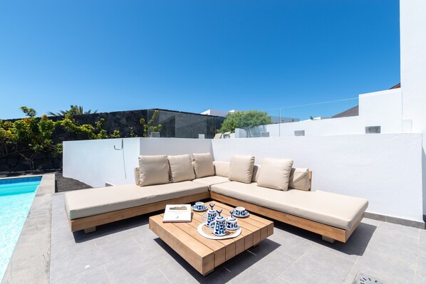 Uma área externa moderna com piscina, mesa de centro de madeira e sofá seccional bege.