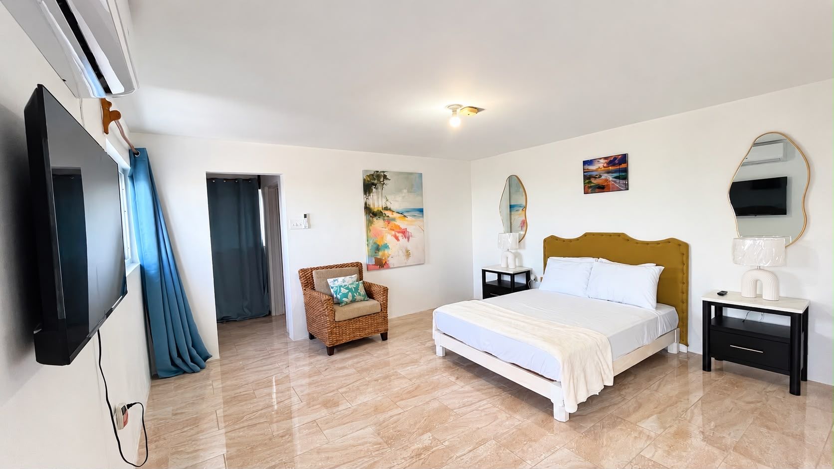 Un dormitorio con cama, una silla, un televisor y obras de arte en las paredes.
