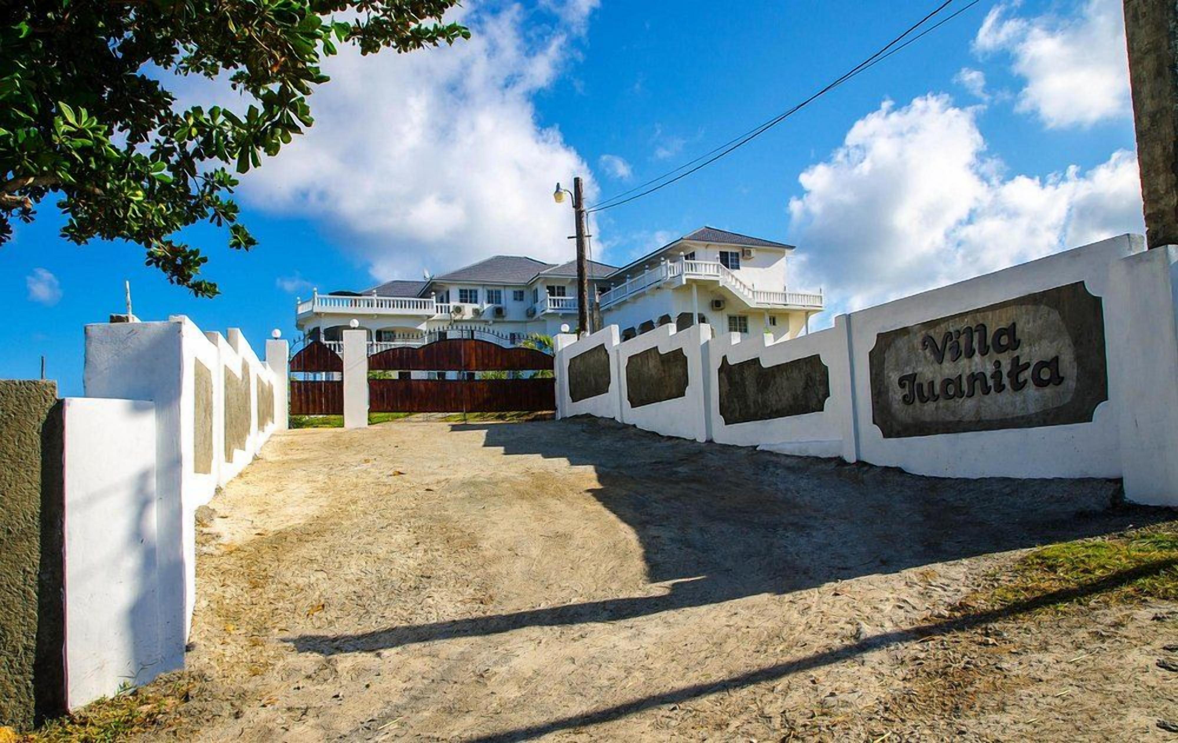 Una entrada portonada a Villa Juanita, cielo despejado y una casa grande al fondo.