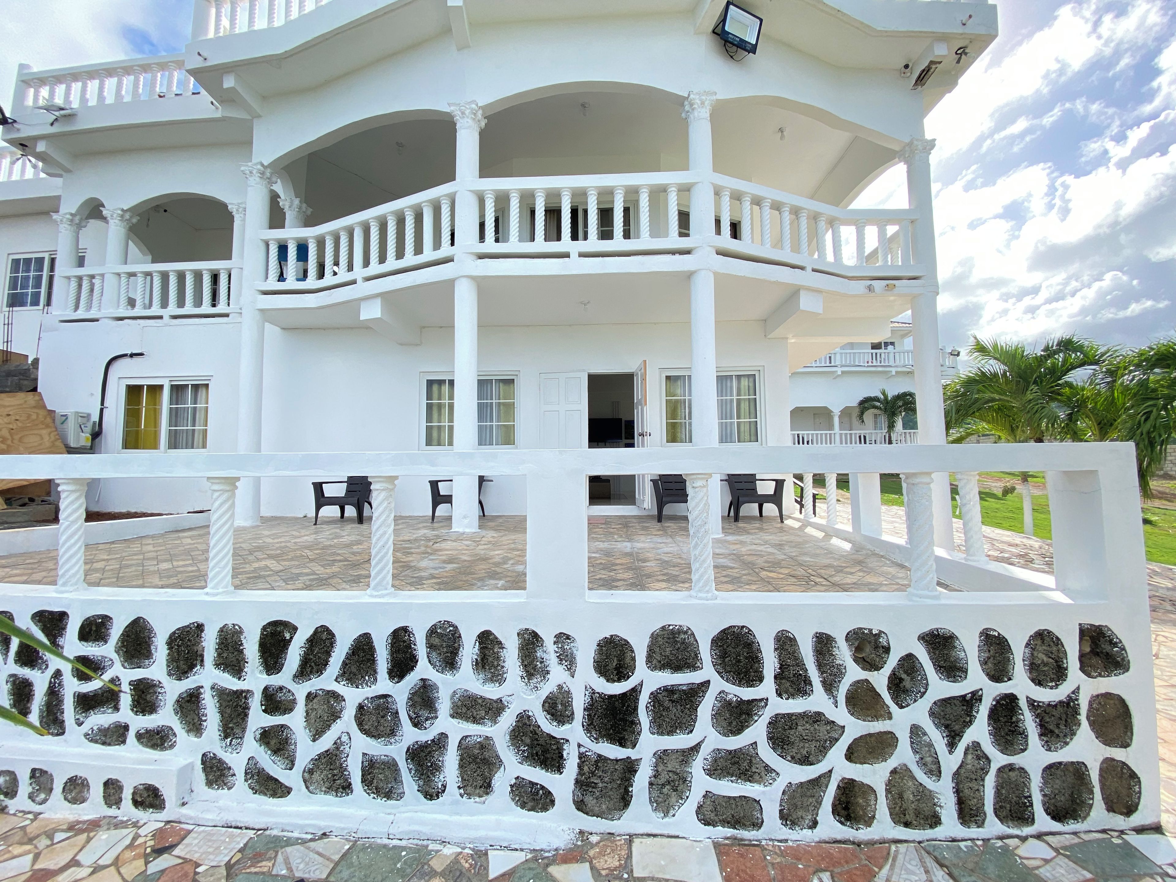 Un edificio blanco de varios niveles con balcones, un muro de piedra y un patio con tejas.