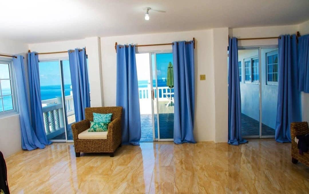 Ein Zimmer mit Meerblick, einem Korbssessel und einer Schiebeglastür.