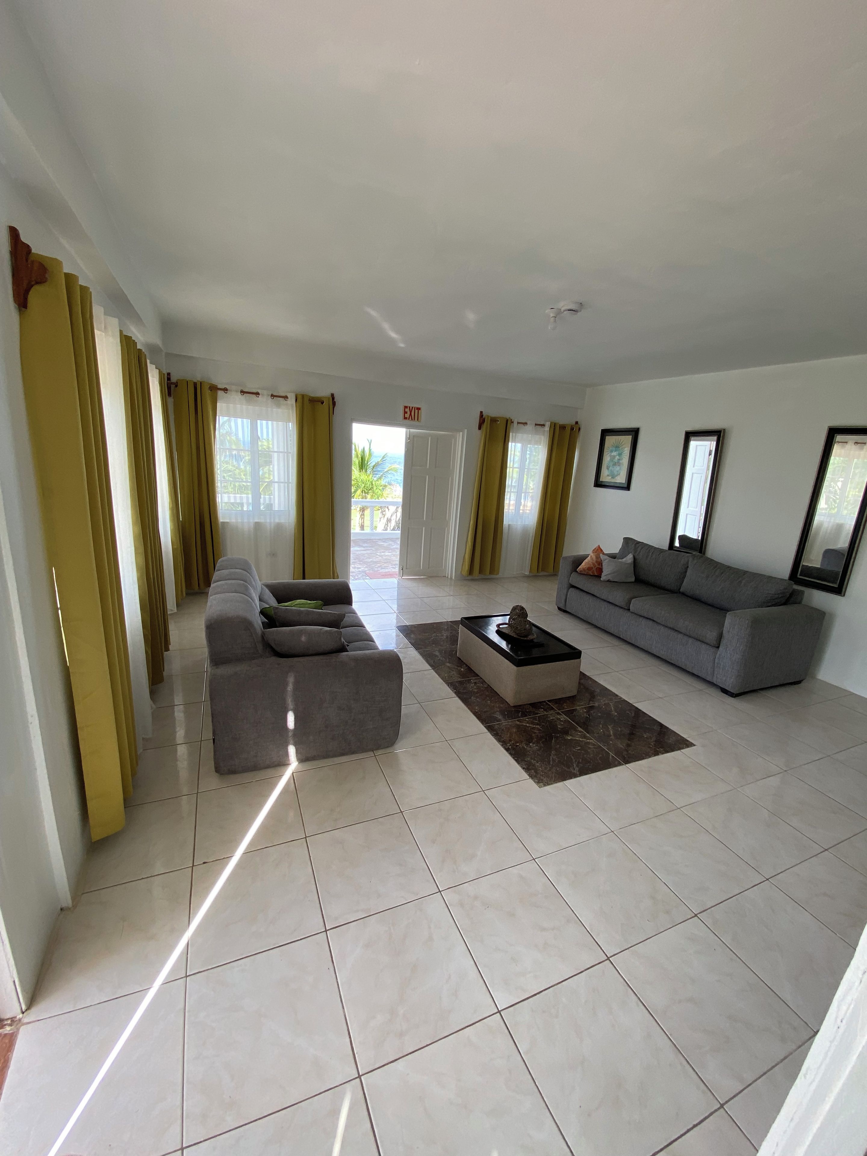 Ein geräumiges Wohnzimmer mit grauem Sofa, passendem Hocker und Couchtisch. Ein Fluchtwegweiser ist an der Wand zu sehen.