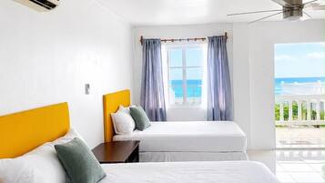Una camera d'albergo con due letti, una ventola a soffitto, un condizionatore d'aria, una finestra con tende e vista sul mare.