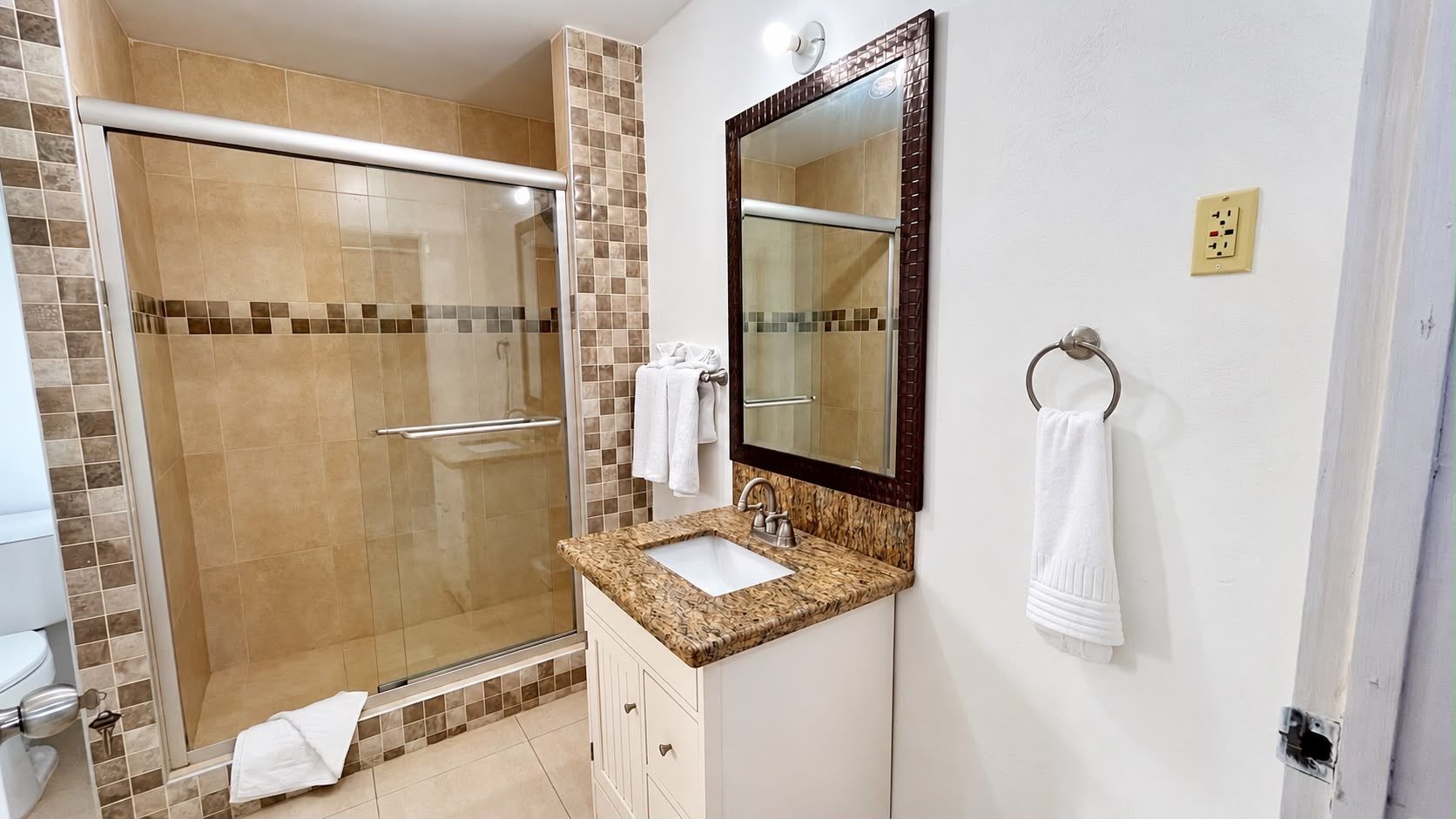 Un baño con cabina de ducha de vidrio, lavamanos con espejo y un perchero para toallas.