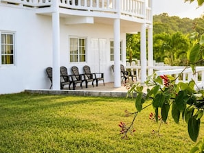 A white building with a covered porch, outdoor seating, and a grassy lawn.