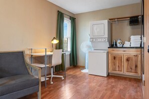 A compact room with a sofa, a desk with a lamp, a washing machine, and a drying rack with towels. - Urban Oasis - Steps from Everything (St. Cloud)