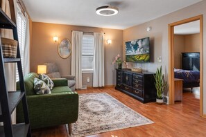 A living room with a green sofa, a black cabinet, a large painting, and a television on the wall. - Urban Oasis - Steps from Everything (St. Cloud)
