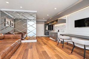 Una cocina moderna con horno integrado, un comedor con mesa y sillas, y una sala de estar con sofá y un separador decorativo.